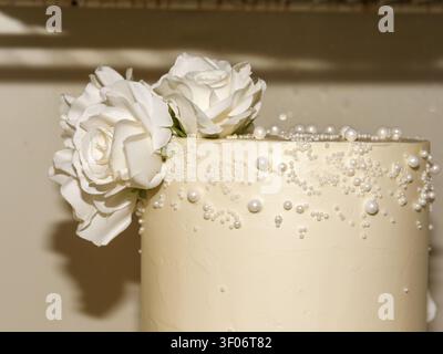 Elegante torta nuziale bianca decorata con perle di zucchero e rose bianche Foto Stock