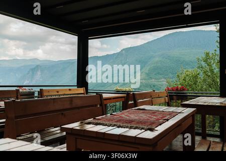 Una accogliente terrazza ristorante in legno che si affaccia su montagne verdi sotto nuvole drammatiche. La seduta all'aperto offre un ambiente tranquillo per cenare e Foto Stock