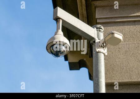 Vista ravvicinata a basso angolo di una moderna telecamera di sicurezza a cupola montata su un palo metallico all'angolo di un edificio. Sorveglianza pubblica all'aperto e monitoraggio CCTV Foto Stock