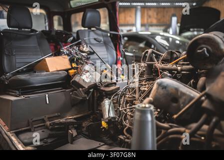 Una scena di officina che mostra l'interno di un veicolo spogliato con componenti del motore esposti e cavi elettrici ingarbugliati Foto Stock