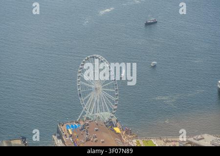 Una grande ruota panoramica bianca sorge su un molo che si estende in acqua blu con diverse barche visibili nelle vicinanze. Foto Stock