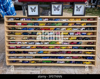 XALO, SPAGNA - 20 GIUGNO 2026. Uno scaffale di legno mostra molte auto giocattolo vintage pressofuse e camion modello in vendita. Due esemplari di farfalle incorniciati sono posizionati in cima Foto Stock