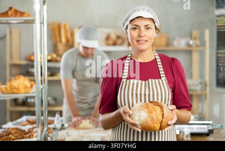 Ritratto della panettiera positiva che tiene in mano un cestino di baguette e pane fresco Foto Stock