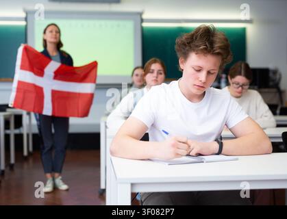 L'insegnante delle scuole superiori racconta agli studenti la Danimarca e tiene in mano una bandiera danese. Foto Stock