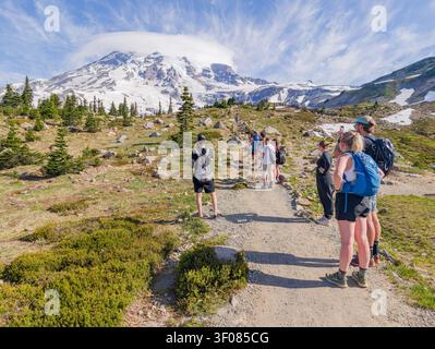 Stato di Washington, Stati Uniti, 24 giugno 2026 - gruppo di escursionisti con zaini in piedi su un sentiero sterrato che guarda il Monte Rainier con un clo lenticolare Foto Stock