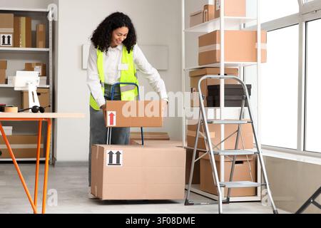 Donna che maneggia scatole di cartone in magazzino con carrello a mano Foto Stock
