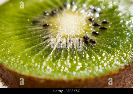 Vista ravvicinata di una kiwi verde vibrante affettata che rivela semi neri e un centro succoso scintillante Foto Stock