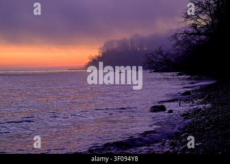Spiaggia rocciosa al crepuscolo con una scogliera boscosa nebbiosa sullo sfondo Foto Stock
