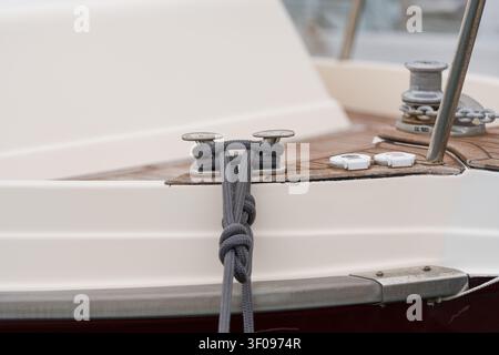 corda legata saldamente a una bita sul ponte di legno di una barca con palo metallico verniciato, configurazione pratica di attrezzatura marina, toni grigi e marroni, vista laterale in primo piano Foto Stock