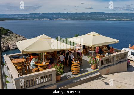 caffè all'aperto rilassato con vista sul mare e persone che cenano e socializzano, ripresa ad angolo alto dall'alto del caffè con tavoli di legno e botti, cemento Foto Stock
