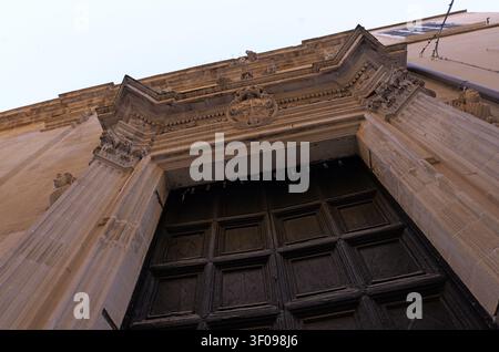 Ingresso della chiesa in stile barocco con decorazioni ornate, colonne in pietra e una grande porta in legno, che celebra il design storico. Italia, lecce, 18 ju Foto Stock