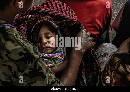 Bambino papuano che dorme pacificamente tra le braccia della madre in mezzo a una folla affollata Foto Stock