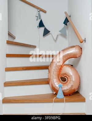 Palloncino numero sei che galleggia su una scala, in una scala interna con gradini e ringhiere in legno, con palloncino numero sei, cappello da festa blu, spago di Foto Stock