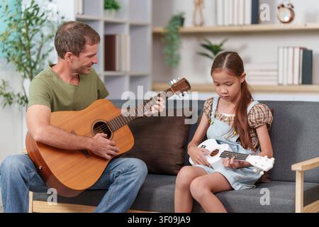 Padre e figlia che suonano chitarra e ukulele a casa per l'educazione musicale Foto Stock