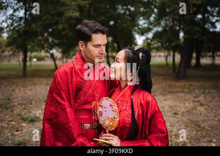 Coppia felice che indossa un tradizionale abito da sposa cinese e si guarda l'un l'altro Foto Stock