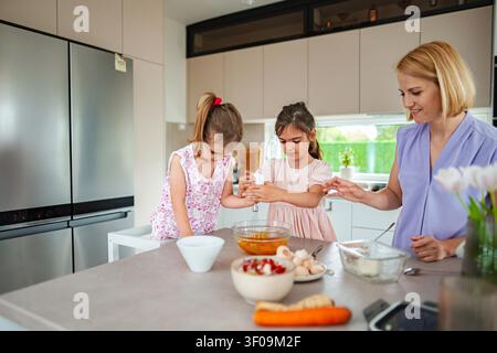 Due bambini e la loro madre si divertono a cucinare insieme al chiuso. Foto Stock