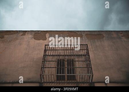 Finestra sbarrata su un muro eroso di una prigione abbandonata Foto Stock