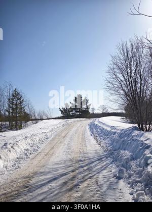 Una strada si scioglie lentamente con l'arrivo della primavera. La neve copre il terreno e gli alberi costeggiano i bordi sotto un cielo luminoso. Foto Stock