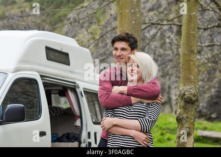 Giovane coppia felice che si abbraccia davanti al camper in campagna Foto Stock