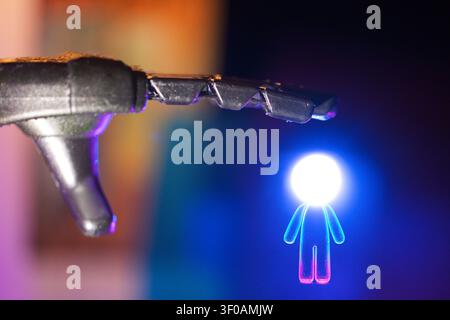 Una mano robotica si estende verso una figura umanoide luminosa, caratterizzata da illuminazione blu e viola, su uno sfondo sfocato Foto Stock