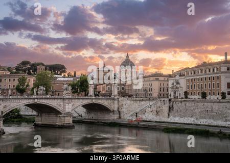 Splendida vista illuminata di Roma, Italia, con la basilica di San Pietro, l'architettura storica, i ponti e il fiume Tevere sotto il cielo serale. Foto Stock