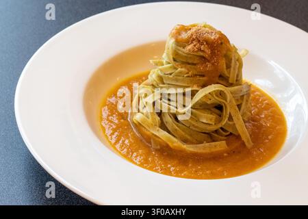 Nido di tagliatelle su salsa di crema di zucca ricoperta di amaretti sbriciolati in un piatto bianco dal bordo largo su superficie grigio scuro, ricetta autunnale italiana Foto Stock