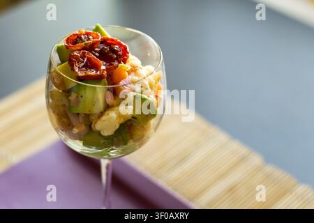 Ceviche di gamberetti e avocado in un bicchiere a stelo con pomodori semi-asciutti, messa a fuoco selettiva su sfondo blu grigio morbido con spazio per il testo Foto Stock