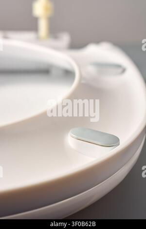 Sedile per WC in plastica bianca con paracolpi in gomma grigia, primo piano su sfondo grigio, vista laterale con messa a fuoco morbida, ricambio per l'hardware del bagno Foto Stock