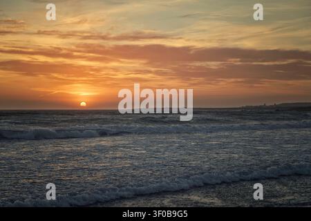 Hå, Norvegia - 14.06.2026: Il sole tramonta all'orizzonte con onde bianche ritmiche che si infrangono su un mare scuro sotto un vasto cielo nuvoloso Foto Stock