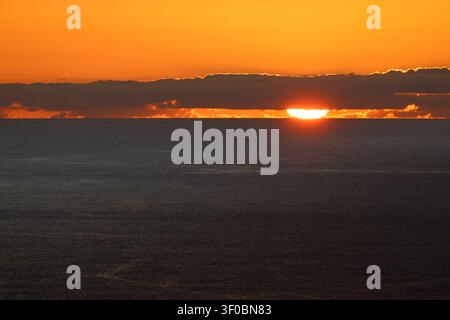 Paesaggio marino minimale con acque calme dell'Atlantico, nuvole stratificate e colori caldi del tramonto che svaniscono nel cielo serale. Foto Stock