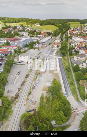Vista aerea di una piccola città con linea ferroviaria, circondata da edifici residenziali e commerciali, incastonata in un paesaggio verdeggiante, Hermann Hes Foto Stock