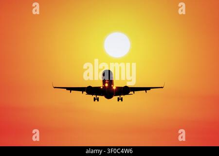 Aereo che vola verso il tramonto in un cielo arancione Foto Stock