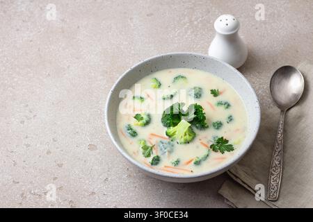 Zuppa cremosa di broccoli fatta in casa con patate, carote e prezzemolo in una ciotola di ceramica su sfondo leggero e texture Foto Stock