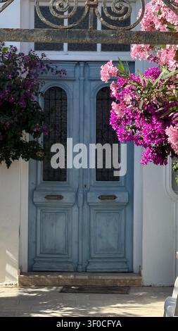 Porta di legno blu accentata da bougainvillea rosa e viola vibranti in una giornata di sole. I colori contrastanti e il design elegante creano un medi pittoresco Foto Stock