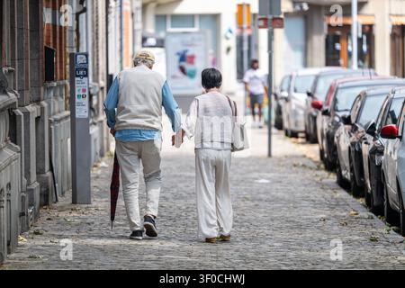 Una coppia anziana cammina mano nella mano lungo una strada acciottolata vicino a Place de l'Yser nel quartiere Outremeuse di Liegi, illustrando la vita quotidiana e un Foto Stock