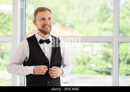 Uomo sorridente abbottonando gilet nero al chiuso Foto Stock