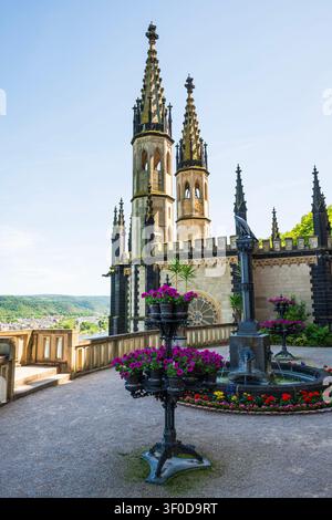 Torri del castello gotico con fontana e fiori viola sulla terrazza con vista Foto Stock