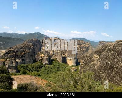 Kalambaka, Grecia – 24 luglio 2024: Paesaggio delle Meteore. Gruppo di torri rocciose nere e gialle in piedi, inserite nella natura verdeggiante di alberi e cespugli sotto Foto Stock