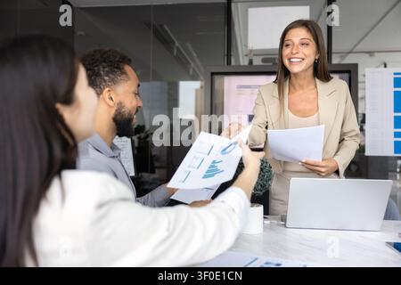 Donna d'affari sorridente che consegna un rapporto a colleghi diversificati Foto Stock