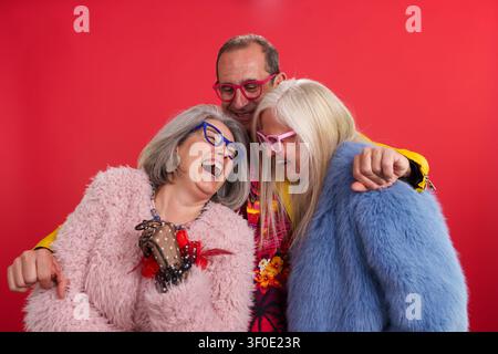 Amici maturi che ridono allegramente indossando abiti colorati e occhiali Foto Stock