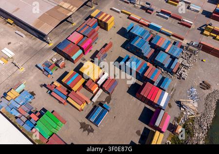 Vista aerea di un cantiere navale pieno di container colorati. I container sono impilati e organizzati a terra. La scena mostra una chiara we Foto Stock