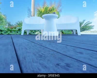 Ambientazione all'aperto con due sedie e un tavolino su un terrazzo con sfondo verde in una giornata soleggiata. Foto Stock