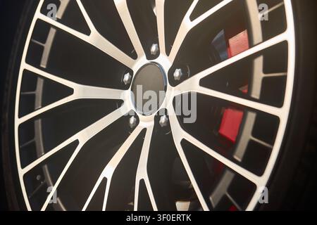 Vista ravvicinata di un cerchio in lega di auto di lusso con raggi argentati intricati su sfondo nero. Pinza del freno rossa vibrante visibile dietro il cerchio. Dettagliato Foto Stock