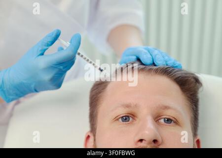 Giovane uomo caucasico che riceve un trattamento di iniezione del cuoio capelluto da parte di un clinico, per affrontare la caduta dei capelli e la cura cosmetica. Primo piano, adatto per dermatologia, trapianto, marketing del benessere Foto Stock
