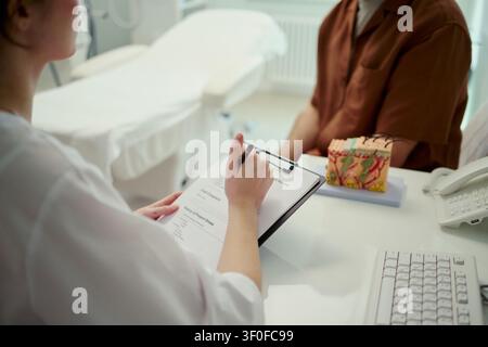 Operatore sanitario donna che esamina un modulo medico con il paziente durante una consultazione in clinica, supportando la diagnosi e la pianificazione delle cure. Utile per i servizi sanitari e il marketing di accoglienza dei pazienti Foto Stock