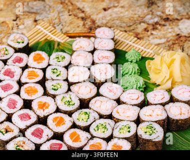 Un vassoio colorato espone una varietà di rotoli di sushi, tra cui tonno, salmone e opzioni di verdure. Il sushi è guarnito con wasabi e zenzero sottaceto, creando un pasto vivace. Foto Stock