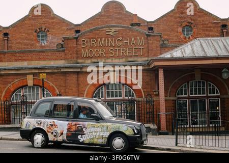Taxi nero tradizionale che passa davanti all'ingresso storico della stazione ferroviaria di Birmingham Moor Street, Regno Unito Foto Stock