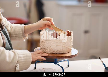 Artista che modella un vaso di ceramica decorativo con rilievo floreale intagliato nello studio di ceramica di una piccola impresa Foto Stock