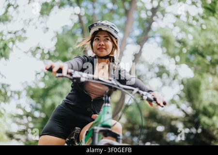 Giovane donna in bicicletta su un sentiero verde, indossa un casco e abiti sportivi e sorride Foto Stock