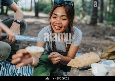 Donna che spalma formaggio fresco su un cracker durante un picnic all'aperto in un bosco con un'amica Foto Stock